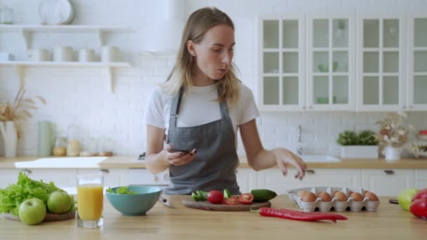 Žena připravuje zeleninu pro bio salát podívejte se na smartphone. — Stock video