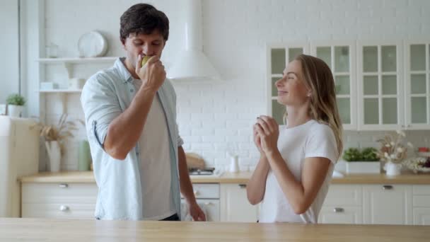 Junges Paar mit Essen zu Hause Küche zusammen. Großaufnahme eines lächelnden Mannes, der mit einer Frau Apfel isst. — Stockvideo