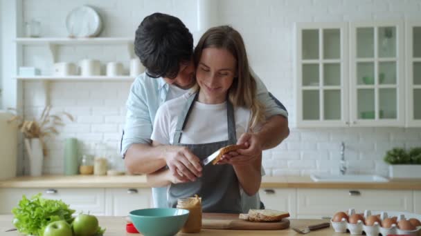 Primer plano feliz pareja cocinar juntos en casa. Hermoso hombre y mujer divirtiéndose. Una joven pareja prepara un sándwich de mantequilla de maní — Vídeo de stock