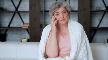 Yaşlı bir kadın rahat bir kanepede dinleniyor, akıllı bir telefonla arkadaşlarıyla konuşuyor. Yaşlı bir bayan, yetişkin çocuklarla cep telefonunda sohbet ediyor..