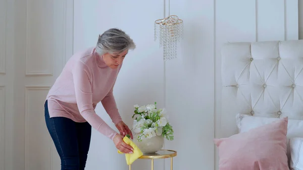 Una anciana limpia una mesa con un trapo en casa. Concepto de trabajo en el hogar y gestión del hogar — Foto de Stock