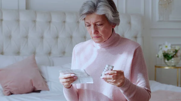 Uma mulher idosa com comprimidos nas mãos e lê um medicamento prescrito. — Fotografia de Stock
