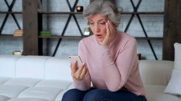 Triste anciana sentarse en sofá celebrar teléfono inteligente se siente decepcionado por sms recibidos malas noticias, dificultades con el uso de dispositivos modernos. — Foto de Stock