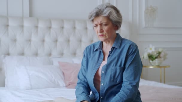 Older woman sit on bed coping with headache — Stock Video