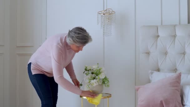 Idős nő letörli az asztalt egy ronggyal otthon. Az otthoni munka és a háztartásirányítás fogalma — Stock videók