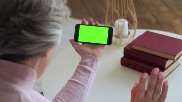 Пожилая взрослая женщина с седыми волосами и видеозвонком на смартфон. Смартфон с зеленым экраном — стоковое видео