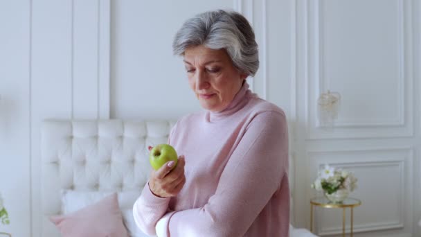 Leende äldre kvinna håller ett grönt äpple i sina händer, hälsosam kost koncept — Stockvideo