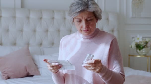 Una anciana con tabletas en las manos y lee un medicamento recetado. — Vídeo de stock