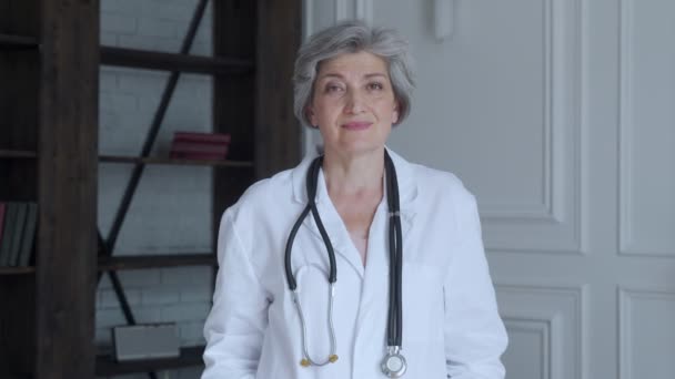 Portrait d'un médecin âgé en robe de chambre, avec stéthoscope sur fond bleu clair des étagères — Video