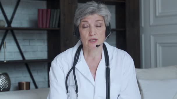 나이든 여성 의사 상담가는 헤드폰으로 화상 통화를 하며 웹 카메라 상에서 화상 회의 전화 채팅으로 온라인 상의 가상 환자와 상담 한다. — 비디오