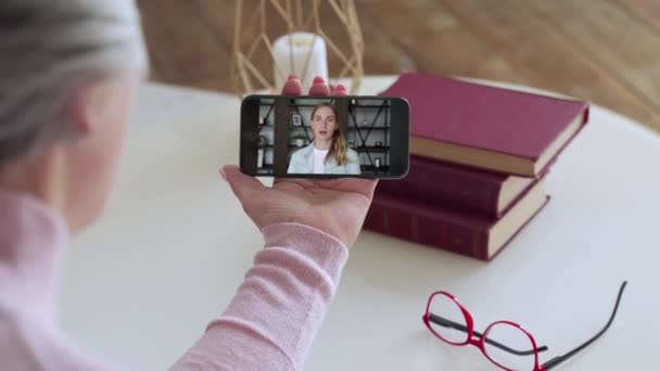 Por encima de la vista del hombro de una anciana videollamada de una hija joven usando un teléfono inteligente. El concepto de videollamada familiar — Vídeos de Stock