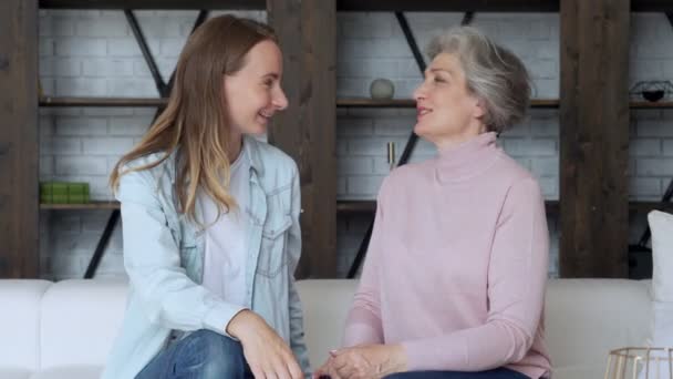 Idős anya és felnőtt lánya otthon a kanapén ülve beszélgetnek és mosolyognak. — Stock videók