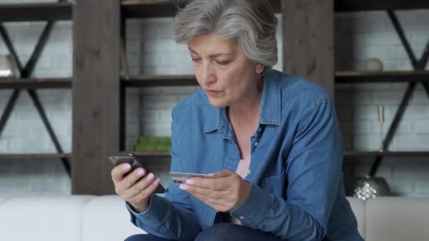 Mulher sênior feliz compras on-line com smartphone e cartão de crédito em casa ou pagar contas de serviços públicos em aplicação — Vídeo de Stock