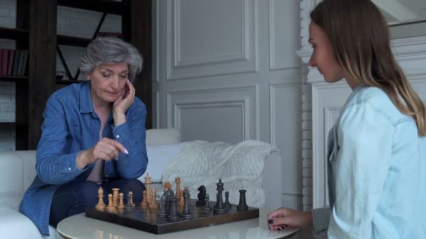 Mor och dotter spelar schack sittandes i soffan i vardagsrummet — Stockvideo