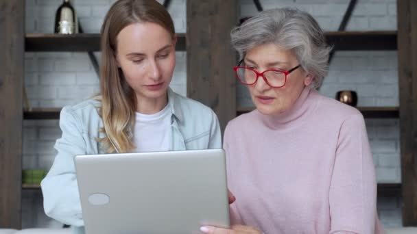 Heureuse génération de femmes de deux ans. Une mère plus âgée et une fille adulte s'amusent à utiliser un ordinateur portable à la maison pour s'asseoir sur le canapé. — Video