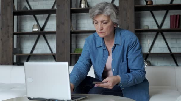 Пожилая женщина с ноутбуком и кредитной картой онлайн покупки дома на диване — стоковое видео