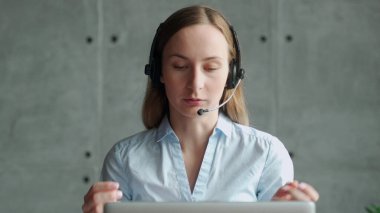 Kablosuz kulaklık takan mutlu bayan yönetici, dizüstü bilgisayara bakıyor, ortaklarla online hoş sohbetler yapıyor, iş yerinde uzaktan çalışıyor.