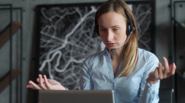 Kablosuz kulaklık takan mutlu bayan yönetici, dizüstü bilgisayara bakıyor, ortaklarla online hoş sohbetler yapıyor, iş yerinde uzaktan çalışıyor.