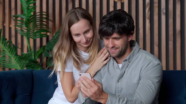 Sonriente pareja joven utilizando el teléfono inteligente juntos en el sofá en casa — Foto de Stock