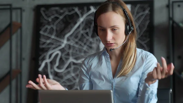 快乐的女经理，戴着无线耳机，看着笔记本电脑屏幕，在网上与合作伙伴客户进行愉快的对话，在工作场所远程工作 — 图库照片