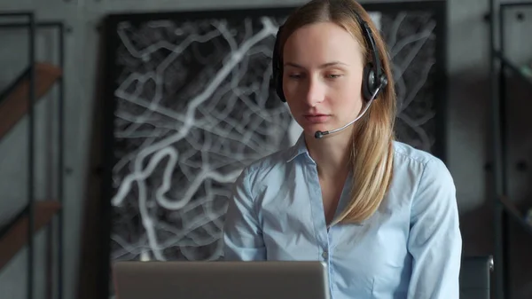 快乐的女经理，戴着无线耳机，看着笔记本电脑屏幕，在网上与合作伙伴客户进行愉快的对话，在工作场所远程工作 — 图库照片