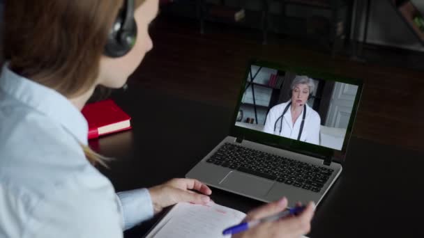 白种人女医生坐在电脑屏幕前，通过互联网给坐在桌旁的病人开药方 — 图库视频影像