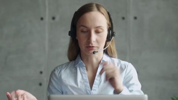 Glad kvinnlig chef bär trådlösa hörlurar, tittar på bärbar skärm, håller trevliga samtal med partners kunder online, arbetar på distans på arbetsplatsen — Stockvideo