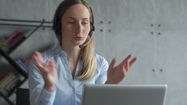 Podnikatelka sedí za stolem, telefonuje, používá sluchátka a notebook — Stock video