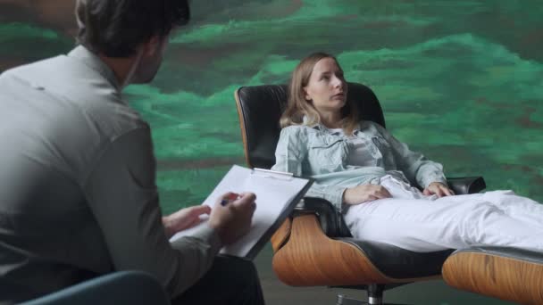 Uno specialista di salute mentale prende appunti quando un paziente parla di problemi mentre è seduto su una sedia — Video Stock