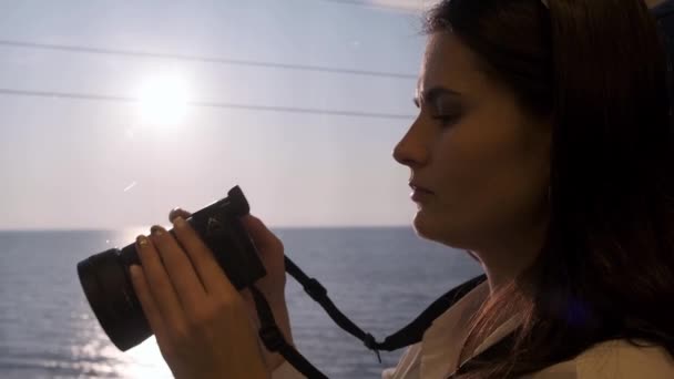A woman rides a train on the background of the sea and takes a photo of a beautiful view from the window. A girl with a camera takes a photo of the sea from the train window.