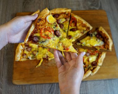   Fast food restoranındaki bir kız, diğer pizzalarla birlikte masanın önünden bir parça pizza alır.. 