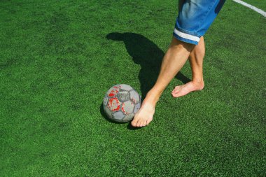 Avrupa futbolu, spor ayakkabı ve yeni bir top için para eksikliği. Ayakkabıve eski bir top olmadan futbolcu, yeşil yeni yapay alanda.   
