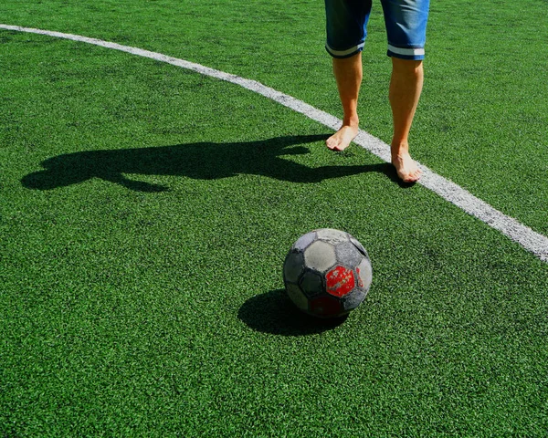 ヨーロッパのサッカー スポーツシューズと新しいボールのためのお金の欠如 緑の新しい人工フィールドで 靴と古いボールのないサッカー選手 — ストック写真