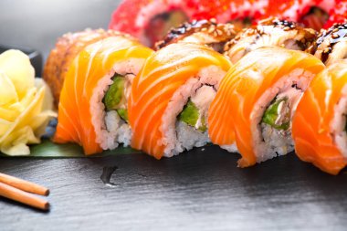 Suşi yakın çekim yapar. Restoranda Japon yemekleri. Siyah kayrak arka plan üzerinde somon, geyik, sebze ve uçan balık havyar ile rulo