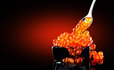 Kaşıkta havyar. Siyah arka plan üzerinde bir kapta Somon havyar