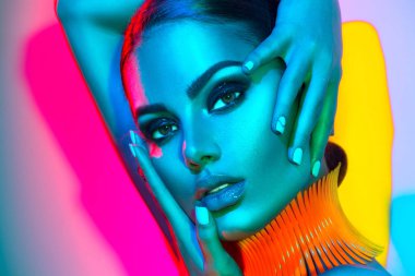 Fashion model woman in colorful bright lights with trendy makeup posing in studio clipart