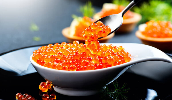 Caviar in a spoon. Salmon caviar in a bowl over black background