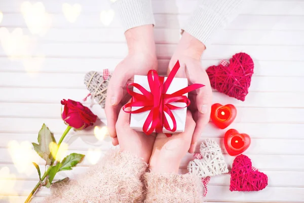 Día de San Valentín. Joven pareja de manos sosteniendo caja de regalo sobre fondo de madera blanca. Concepto de amor —  Fotos de Stock