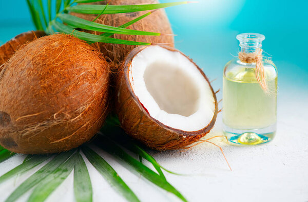 Coconut oil in a bottle with coconuts and green palm tree leaf o