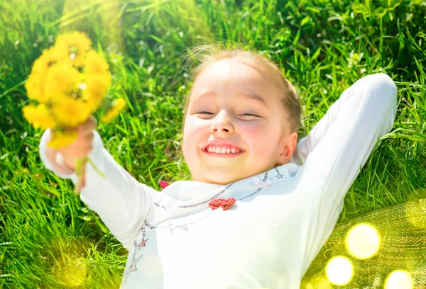 Портрет улыбающейся маленькой девочки, лежащей на зеленой траве с бу — стоковое фото