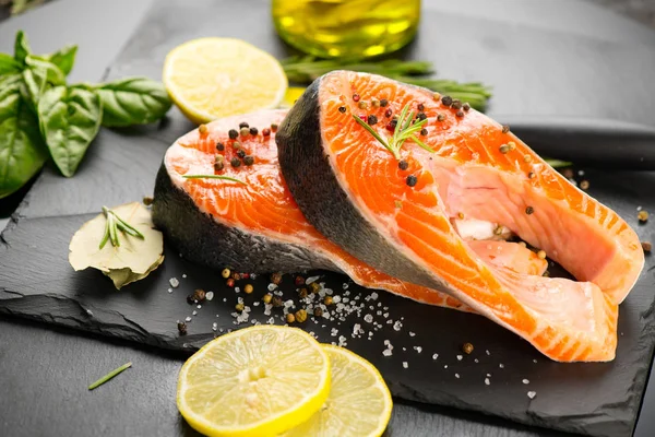 Salmon. Raw trout fish steak with herbs and lemon on black slate — Stock Photo, Image