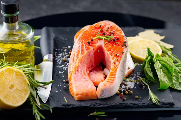 Lachs. rohe Forellenfischsteak mit Kräutern und Zitrone auf schwarzem Schiefer Stockbild