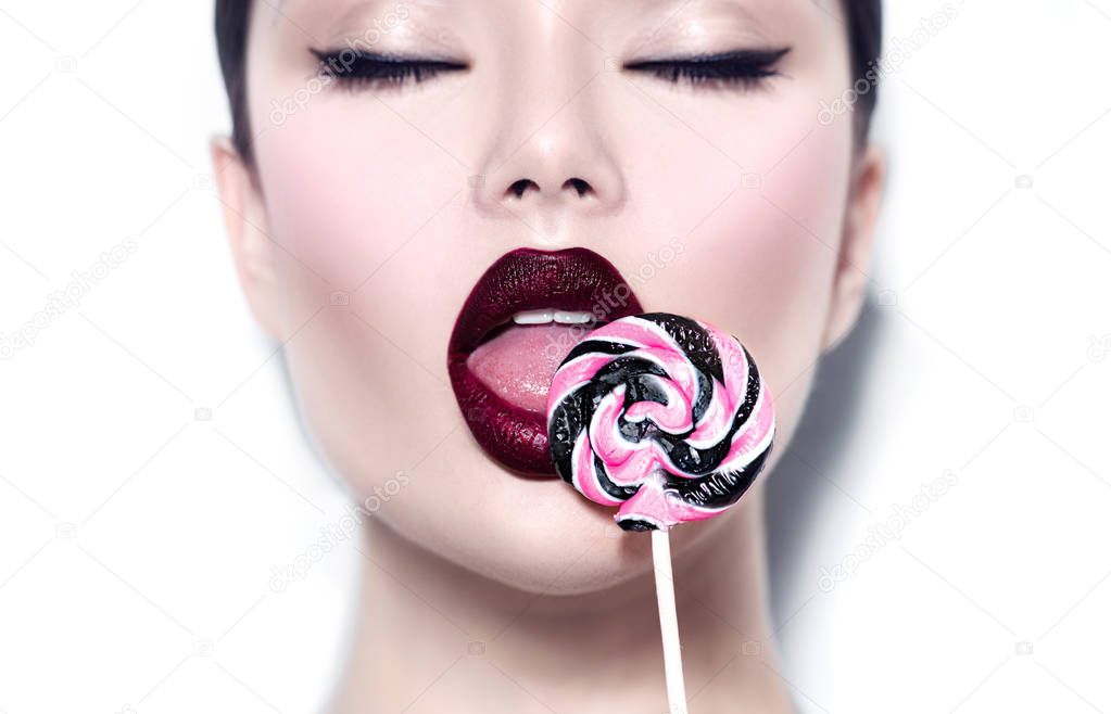 Sexy beauty girl eating lollipop. Glamour model woman licking sweet colorful lollipop candy over white background
