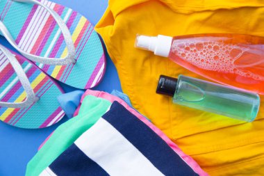 Tatil, seyahat veya yolculuk için hazırlanıyor. Planlama seyahat. Rezervasyon otel. Dolar, terlik ve suncream mavi zemin üzerine sarı kot pantolon. Instagram üstten görünüm