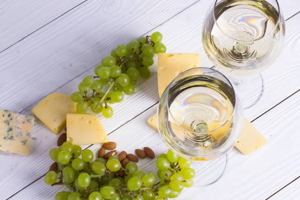 Glass of white wine with snacks - various types of cheese, figs, nuts, honey, grapes on a wooden boards background. Top view