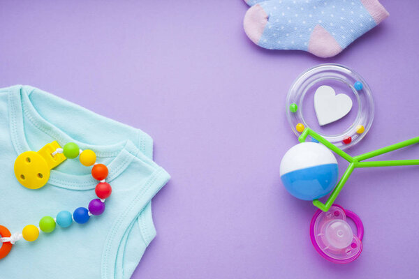 Baby yellow booties. Children's shoes and toys on purple background. Newborn. Top view