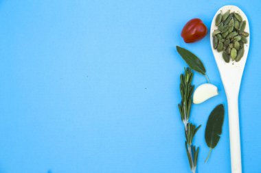 Pişirme sıcak baharatlı yemek kavramı. Tahta kaşık ve bir ışık mavi backhround, üstten görünüm, taze otlar kiraz domates kuru fasulye alanı Kopyala