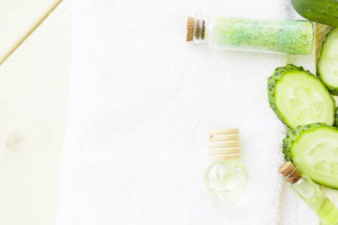 Salatalık ev spa ve saç bakım kavramı. Dilimlenmiş salatalık, petrol şişe, kavanoz maskesi, banyo havlu. Beyaz tahta arka plan. Portre