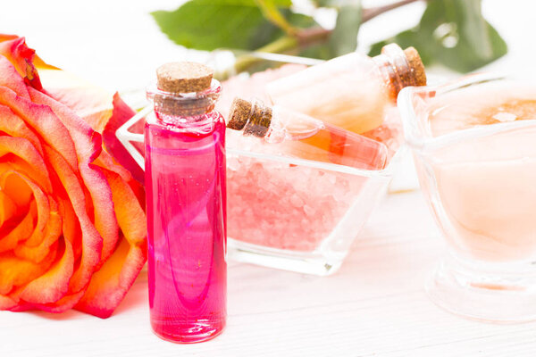 Spa and wellness setting with rose flower, sea salt, oil in a bottle on wooden white background closeup