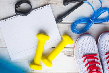 Diyet Zayıflama kilo kaybı kavramı zamanı. Spor, fitness, elma, spor ayakkabıları, şişe su ve sarı ağırlık beyaz ahşap zemin üzerinde